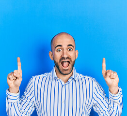 Young bald man pointing up with fingers celebrating crazy and amazed for success with open eyes...
