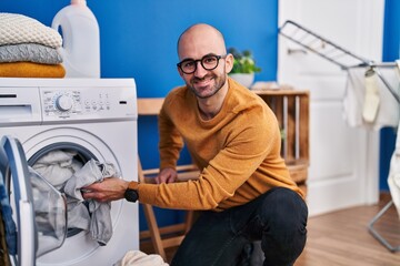 Young man smiling confident washing clothes at laundry room