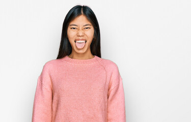Fototapeta premium Beautiful young asian woman wearing casual winter sweater sticking tongue out happy with funny expression. emotion concept.