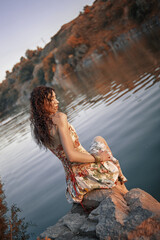 an attractive young girl with wet hair sits on the rocks on the shore of a picturesque lake. romantic image