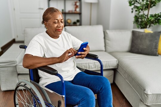 Senior african american woman using smartphone sitting on wheelchair at home