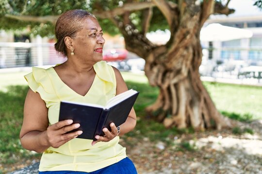 Senior african american woman reading book sitting on the bench at the park.