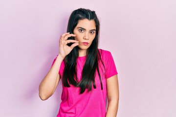 Young hispanic girl wearing casual pink t shirt mouth and lips shut as zip with fingers. secret and...