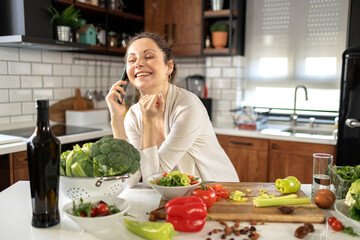 Pregnant woman in the kitchen prepare vegetarian food and use mobile phone and smile