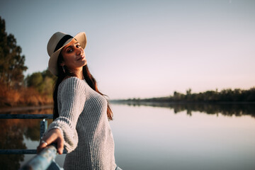 Hispanic brunette woman with hat relaxing on the shore of a river next to a pier