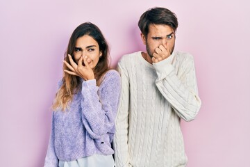 Young hispanic couple wearing casual clothes smelling something stinky and disgusting, intolerable smell, holding breath with fingers on nose. bad smell - obrazy, fototapety, plakaty