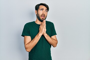 Young hispanic man wearing casual white tshirt begging and praying with hands together with hope...