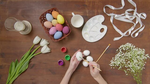 Top view of a table with items to create a composition for Easter. Women's hands paint Easter eggs with colored paint. Church holiday-Easter