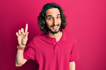 Young hispanic man wearing casual clothes smiling with an idea or question pointing finger up with happy face, number one