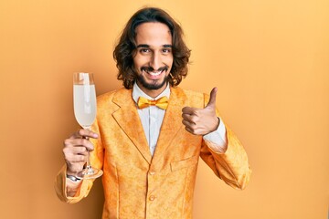Young hispanic man wearing nerd elegant style drinking a glass of sparkling champagne smiling happy...