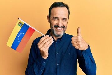 Middle age hispanic man holding venezuelan flag smiling happy and positive, thumb up doing excellent and approval sign - obrazy, fototapety, plakaty