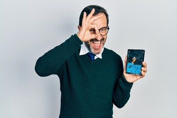 Middle age hispanic man holding hdd disk smiling happy doing ok sign with hand on eye looking through fingers