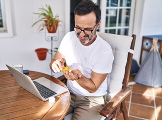 Middle age man using laptop taking pills at terrace home