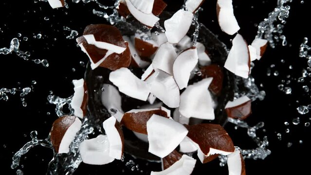 Super slow motion shot of rotating exploded coconut cuts and splashing water on black at 1000fps.