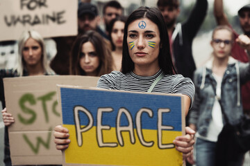 Peace young people activists protesting against war against Ukraine. Focus on a young woman holding...