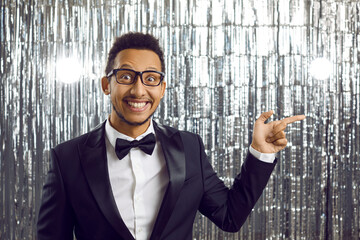 Portrait of cool funny young man in suit pointing his finger to side on silver background. Close up...