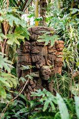 Stone carved totem with  human face among tropical plants