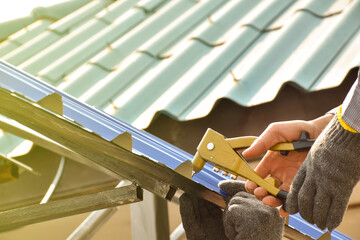 A male mechanic installs the roof of the house with all the equipment used for installation with skill