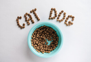 A blue bowl with dry food on a white background next to the inscription from the feed. Pets. Animal feed.