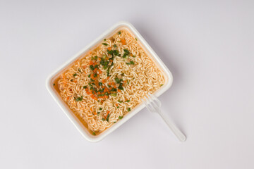 instant noodles with a plastic fork, vegetables and hot spices in a container with water on a white background. fast food concept