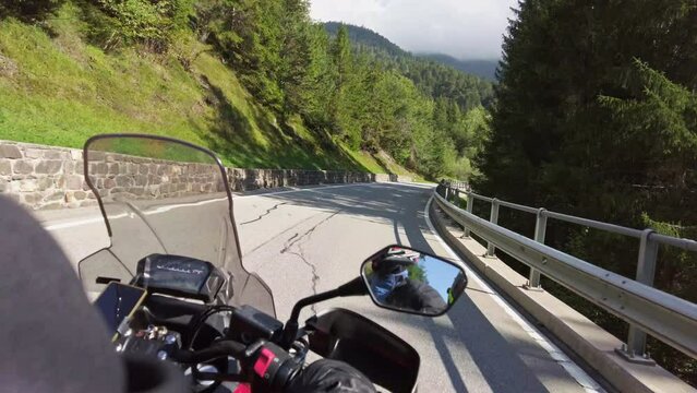 POV Biker rides on motorbike by scenic sunny mountain road in Swiss Alp. Motorcyclist on motorcycle goes between mountain valley by landscape highway. Steering wheel view. First-person view. Moto trip