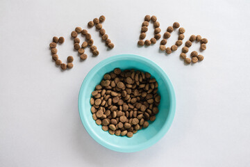 A blue bowl with dry food on a white background next to the inscription from the feed. Pets. Animal feed.