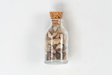 Small rocks in glass bottle with cork stopper isolated on white background, for remembrance, broken...