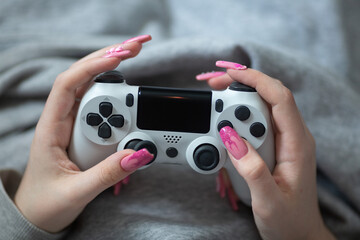 In the hands of a young girl, a joystick with which she plays a video game, a gray sweatshirt on the girl, a pink manicure with ornaments on her long nails, beads, a figurine, stickers, a drawing