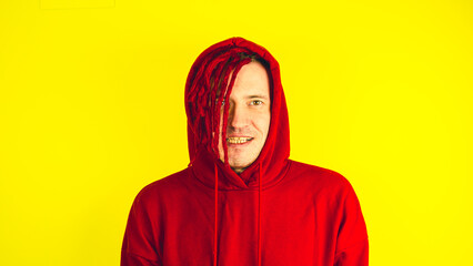 Young man with red dreadlocks in hood looking at camera. Portrait of handsome male smiling and expressing positive emotions.