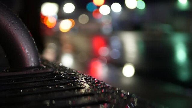 Car traffic lights bokeh, reflection on bus stop bench in rainy weather. Water rain drops on wet metal, city street in Clifornia, USA. Rainfall at night. Defocused abstract Seamless looped cinemagraph