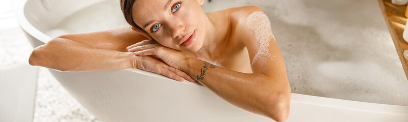 Attractive young woman feeling tired, leaning on bathtub side, bathing while relaxing at spa...