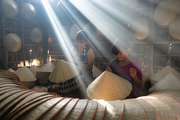vietnamese woman making with her grandchild a traditional conical hat at her home