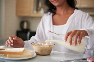 Woman pouring nondairy milk in bowl with granola when making breakfast