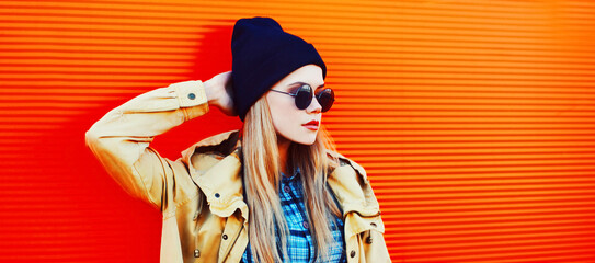 Fashion portrait of blonde young woman in black sunglasses and hat on colorful orange background