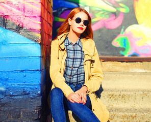 Fashion portrait of beautiful stylish blonde young woman on city street over colorful graffiti background