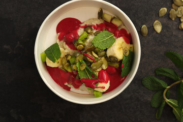 Vegan food. Breakfast oatmeal porridge with banana, strawberry sauce, pumpkin seeds and mint on a dark background in an eco paper box. Healthy balanced food. Top view, overhead, banner