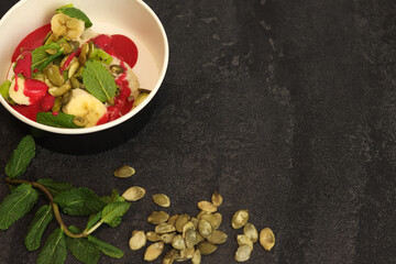 Vegan food. Breakfast oatmeal porridge with banana, strawberry sauce, pumpkin seeds and mint on a dark background in an eco paper box. Healthy balanced food. Top view, overhead, banner