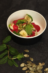 Vegan food. Breakfast oatmeal porridge with banana, strawberry sauce, pumpkin seeds and mint on a dark background in an eco paper box. Healthy balanced food. Top view, overhead, banner