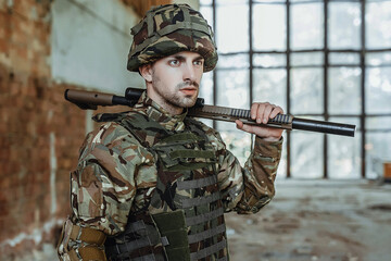 Male soldier in uniform wears a big gun in his hands standing in derstroy building.
