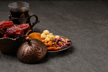 Ramadan Kareem. Dates in traditional middle-eastern brass bowl, nut mix and tea cup in brass cup holder at stone surface. Holy Month concept low key copy space