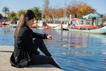 Young pretty girl sitting on the ground near the water canal in Aveiro, Portugal.