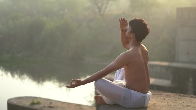 Young indian boy doing yoga early in the morning, boy doing anulom vilom near a river.