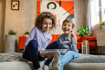 Siblings brother and sister boy and girl or children friends using digital tablet at home i room to watch video make a call or play online games leisure family concept real people copy space