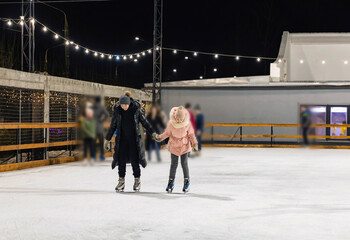 mother and daughter skate on the ice rink in the evening