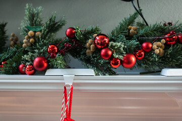 A decorated white Christmas mantle with pine garland and strung red ball ornaments