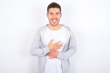 young caucasian man wearing casual clothes over white background keeps hands crossed, laughs out loud at good joke, wears casual clothes.