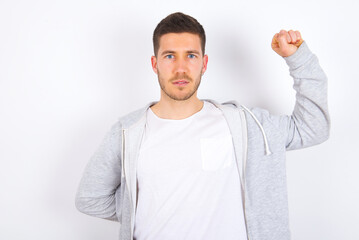 young caucasian man wearing casual clothes over white background feeling serious, strong and rebellious, raising fist up, protesting or fighting for revolution.