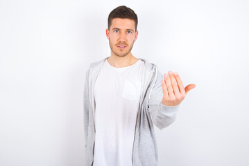 young caucasian man wearing casual clothes over white background, inviting you to come, confident and smiling making a gesture with hand, being positive and friendly.