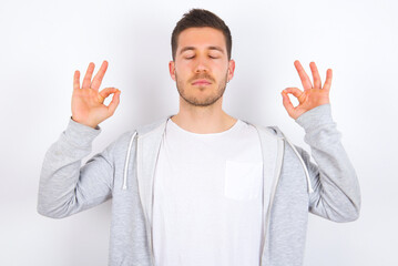 young caucasian man wearing casual clothes over white background doing yoga, keeping eyes closed,...