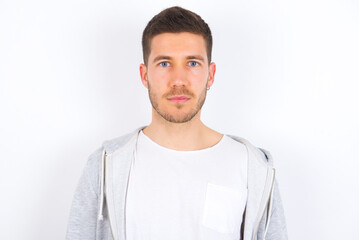 Joyful young caucasian man wearing casual clothes over white background looking to the camera, thinking about something. Both arms down, neutral facial expression. - obrazy, fototapety, plakaty